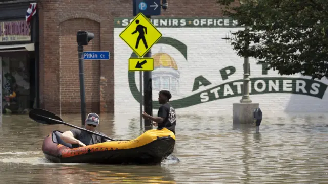 A man in an inflatable kayak passes by a pedestrian in the flood waters of Main Street in Montpelier, Vermont, USA, 11 July 2023