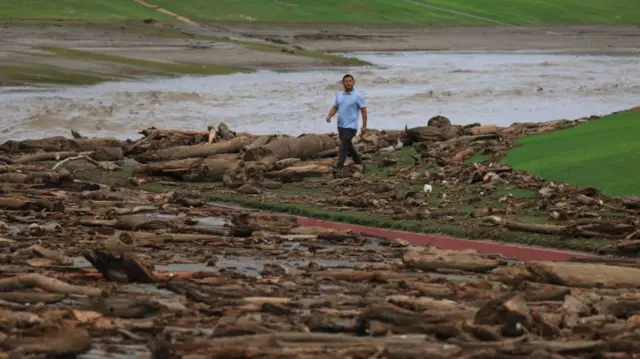 A worker from the Coachella Valley Water Department surveys the debris flow following heavy rains from Tropical Storm Hilary, at Thunderbird Country Club in Rancho Mirage, California