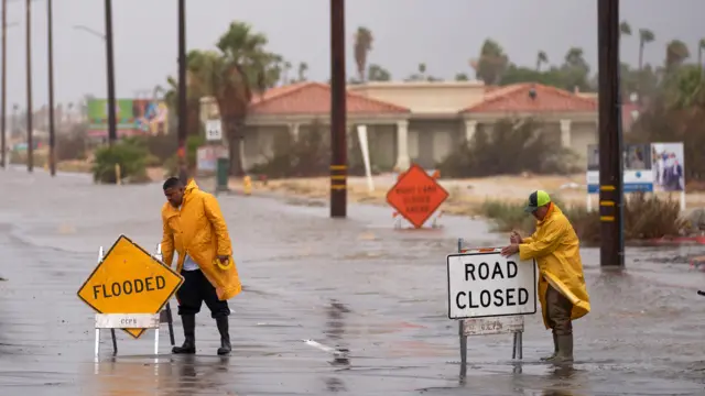 Public works employees set up signs to close a road due to flooding as Tropical Storm Hilary arrives in Cathedral City, California