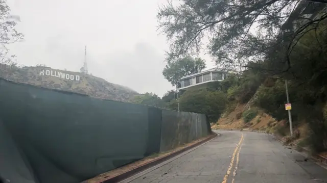 A road under the Hollywood sign lined with a protective barrier