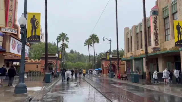 People in plastic ponchos wander the street in the rain