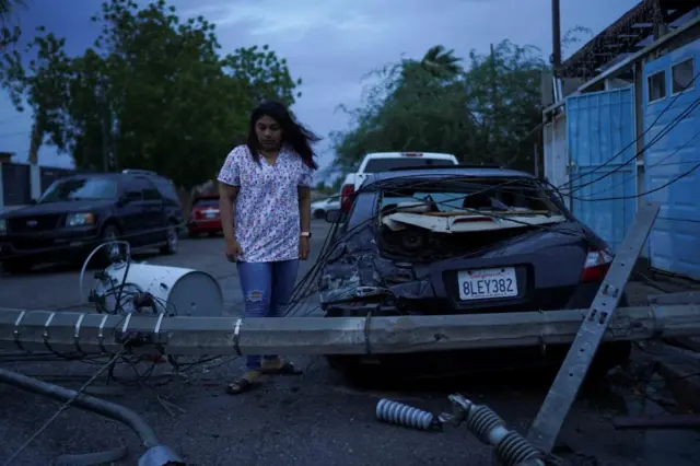 Laura Elizalde Reyes looks at a light pole that hit her car as Tropical Storm Hilary hits Baja California state, in Mexicali, Mexico.