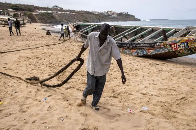 A fisherman pulls a rope as they try to move a beached pirogue in Dakar on 9 August, 2023, in which migrants lost their lives