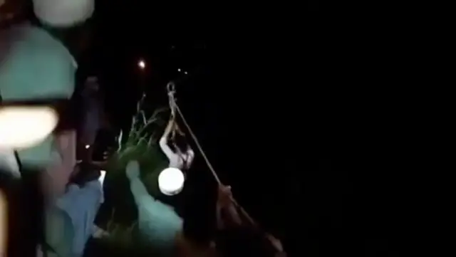 Rescuers pull a boy attached to a harness to safety at night