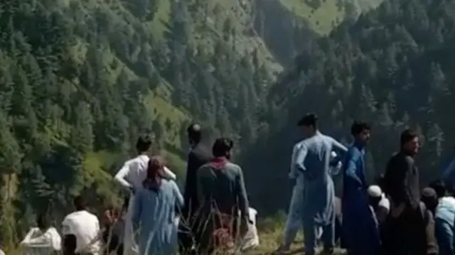 A crowd stands on one side of a valley