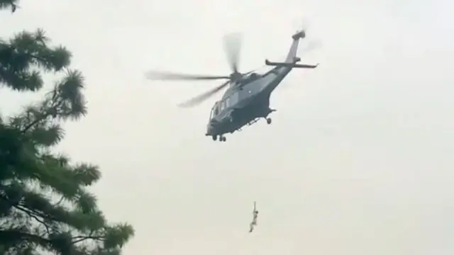 A photo taken from the ground of a person dangling from a helicoper