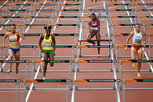 Masai Russell hits a hurdle as three athletes run ahead of her during the 100m hurdles semi-finals.