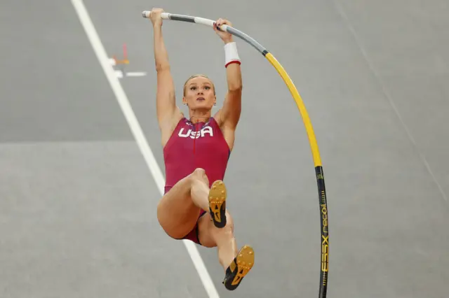 Katie Moon is mid-air with two hands on the bending pole as she launches herself off the ground.