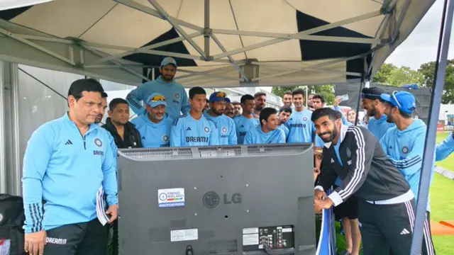 The team dressed in blue watch a TV beside a field