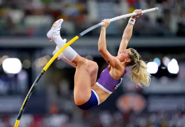 Molly Caudery in mid-air and clutches the pole with both hands