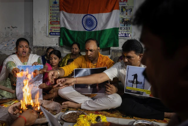 A group of people holding images of the spacecraft performing a ritual in front of a fire, with the Indian flag in the background