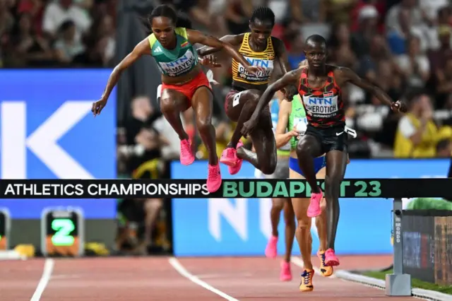 Faith Cherotich jumps over the hurdle with competitors jumping behind her in the Women's 3,000m steeplechase