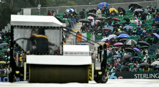 Spectators watch on from under umbrellas as the 'Blotter' is driven across the covers as play is delayed due to rain