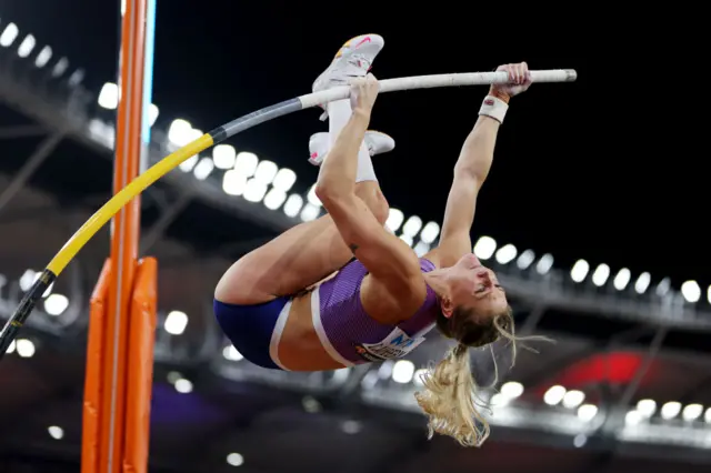 Molly Caudery is upside down in the air and holds onto the pole with two hands