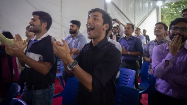 Men stand, clapping and cheering