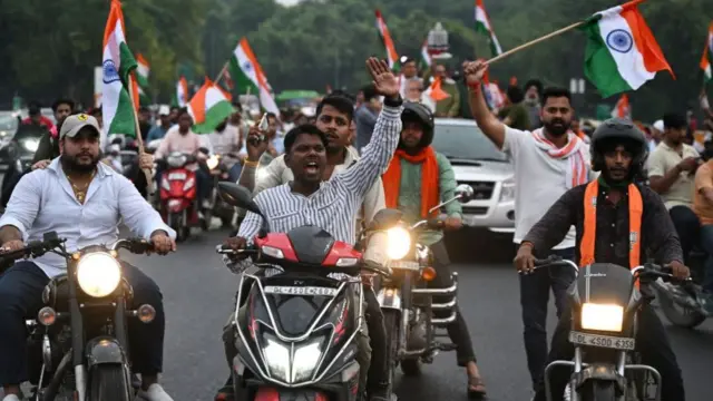 Men on motorbikes wave flags and cheer