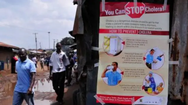 People walk past a kiosk where a poster giving information on how to prevent Cholera is displayed in the Kibera area of Nairobi on May 20, 2015. At least 65 people are confirmed to have died in a nearly five-month-old cholera outbreak in Kenya, with infections also continuing to rise in the capital Nairobi,