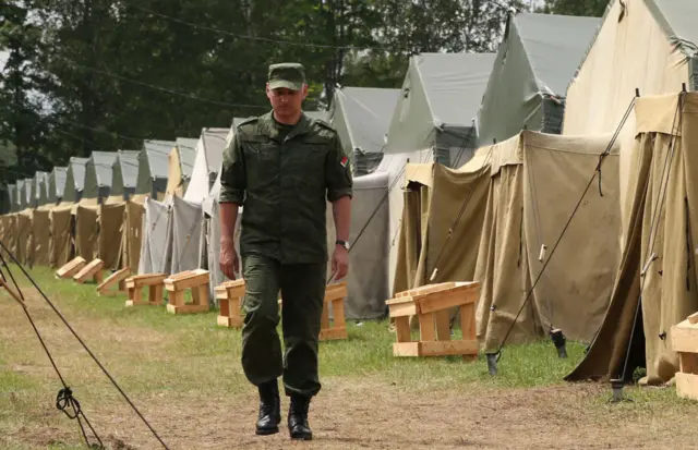 A Belarusian soldier walks past a row of tents prepared for Wagner fighters