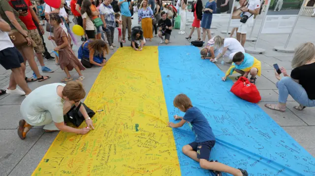 People write on a giant Ukrainian flag in Warsaw