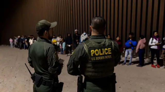 US border patrol officers check the identity of migrants before they can get into a bus for a processing center after they crossed the border between the United States and Mexico