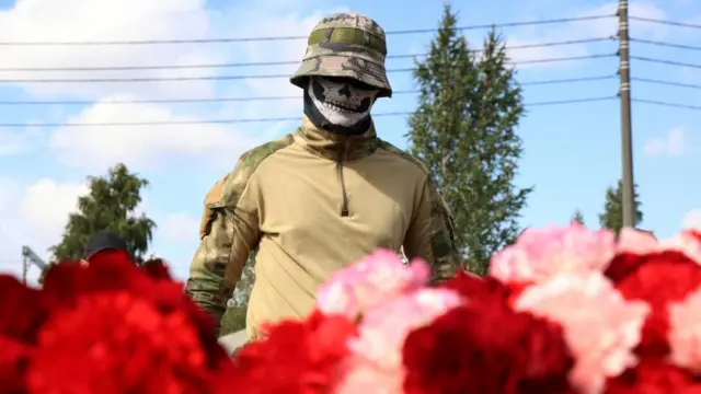 Wearing a mask, a presumed fighter of the Wagner mercenary group visits a makeshift memorial