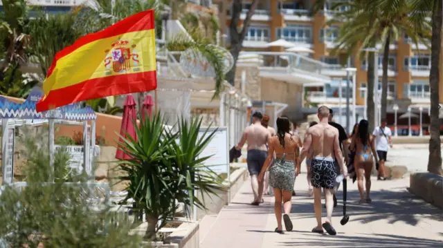 Tourists walk by the seafront at Magaluf beach, where a Spanish flag is being flown outside a cafe