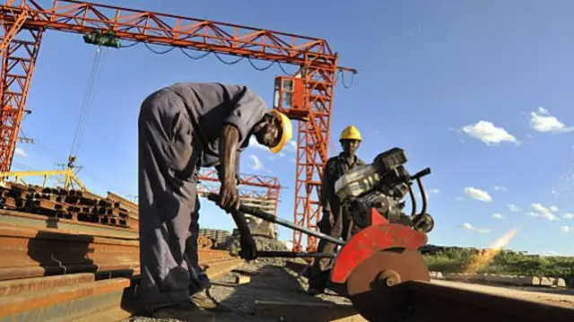 African workers use a circular saw to cut a length of steel rail track at the Kathekani T-girder and rail sleeper manufacturing plant which makes parts for the construction of the new Mombasa-Nairobi Standard Gauge Railway (SGR) line in Tsavo, Kenya, on Wednesday, March 16, 2016