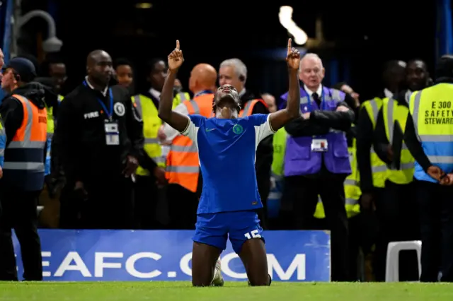 Nicolas Jackson kneels on the floor and points to the sky in celebration.