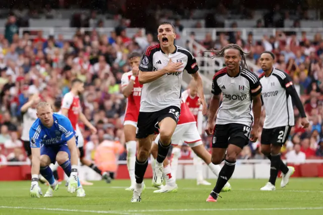 Palhinha pats the crest on his chest as he runs to the corner to celebrate with the away fans/ Ramsdale looks on after conceding.