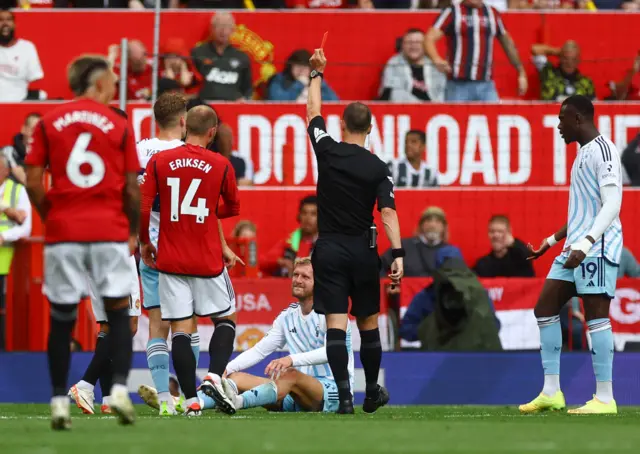 Worrall sat on the floor is shown a red card by the ref.