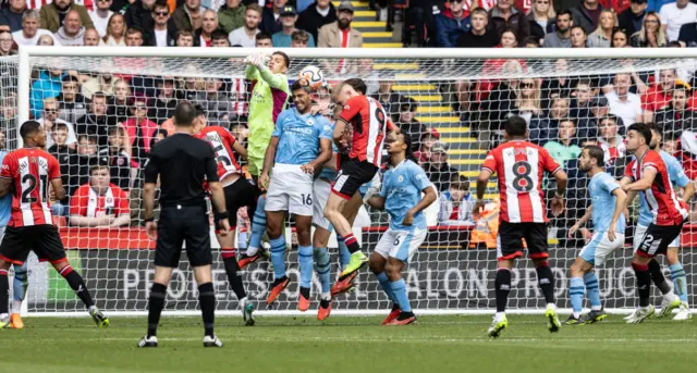 Ederson punches the ball in the middle of a crowded penalty area.