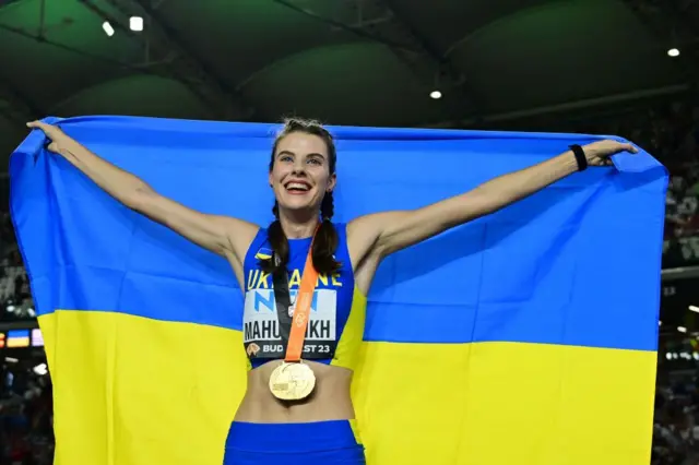 Yaroslava Mahuchikh holds the Ukrainian flag wearing a gold medal