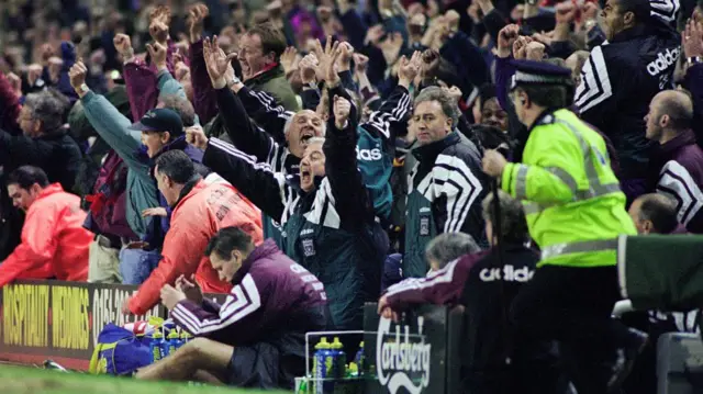 Liverpool bench celebrates as Kevin Keegan drapes over the hoardings at Anfield in 1996