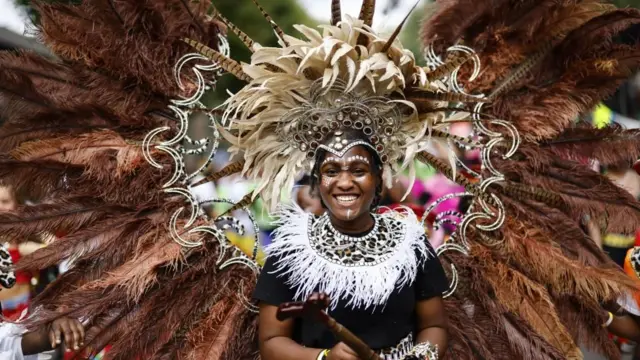 A person smiles wearing an extravagant feathered costume