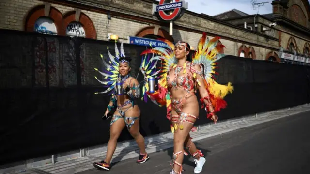 Two performers walk past a tube stop