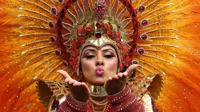 A woman in an elaborate headpiece blows a kiss