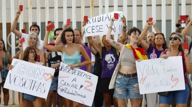 A group of protestors holding up red cards and banners against Rubiales