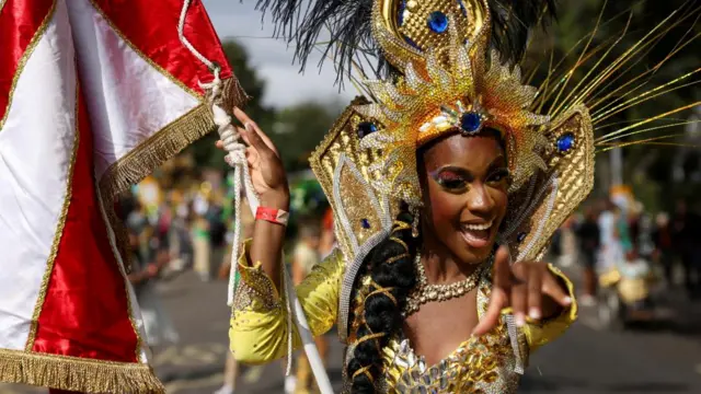 A woman in a gold costume smiles as she points to the camera