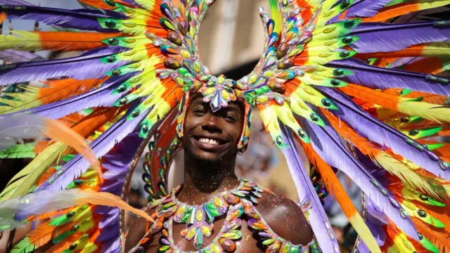 A man in rainbow feathers and matching jewels