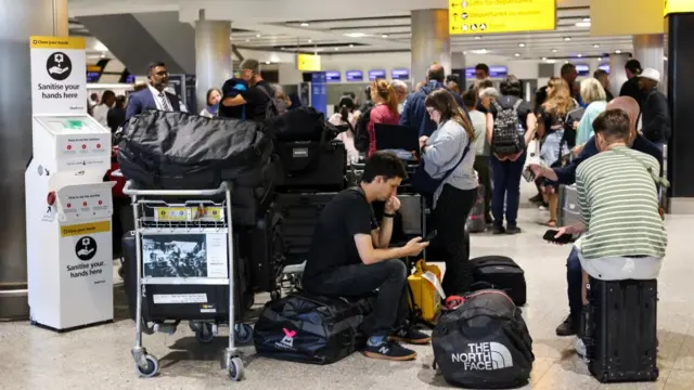 Travellers wait near the British Airways check-in area at Heathrow Airport