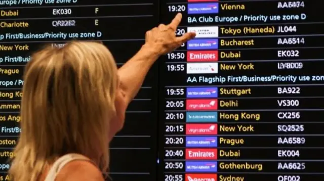 Woman points at departure boards at Heathrow Airport