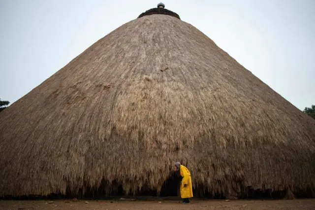 A traditional guard stands in front of one of the buildings belonging to the Kasubi Royal Tombs in Kampala, Uganda on June 13, 2023