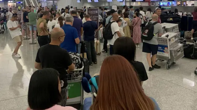 A crowd of people queue by the Qatar service desks at an airport