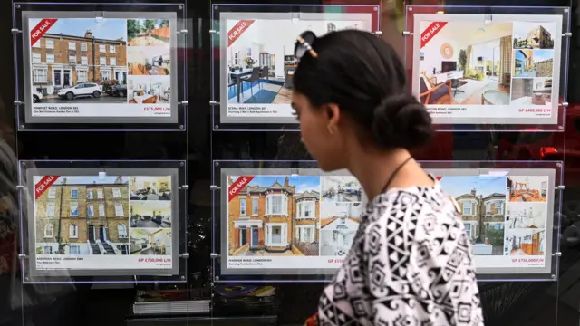 A young woman looks at properties for sale in the window of an estate agents' office