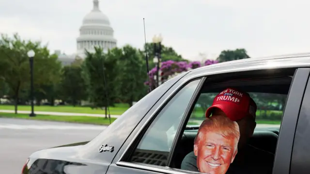 A person holds a Trump mask inside a vehicle in Washington DC