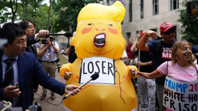 A demonstrator in a costume depicting Trump as a big baby, with a 'loser' sign