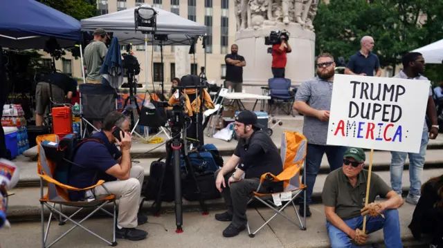 Members of the media and protesters gather outside the E. Barrett Prettyman United States Courthouse