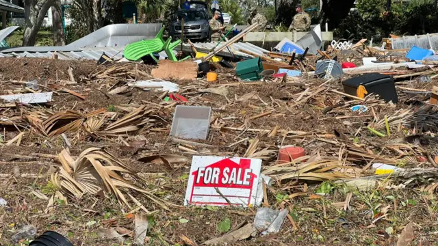 A 'For Sale' sign is seen among the debris of a destroyed building