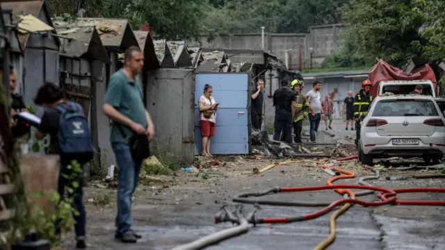 People stand outside garages that back onto a street, debris scattered around them