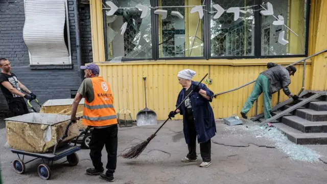 A woman sweeps a footpath, others around her transport goods and survey damage